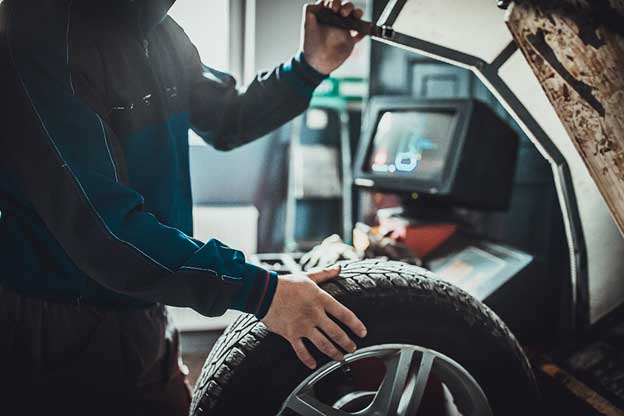 View of a certified auto repair technition calliborating a tire for alignment with a monitor in the background showing the data from OEM.
