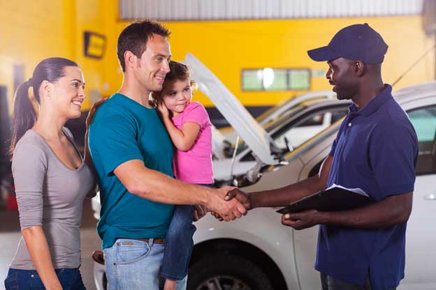 A happy mother and father with their little girl standing in a collision center and shaking hands with a mechanic.