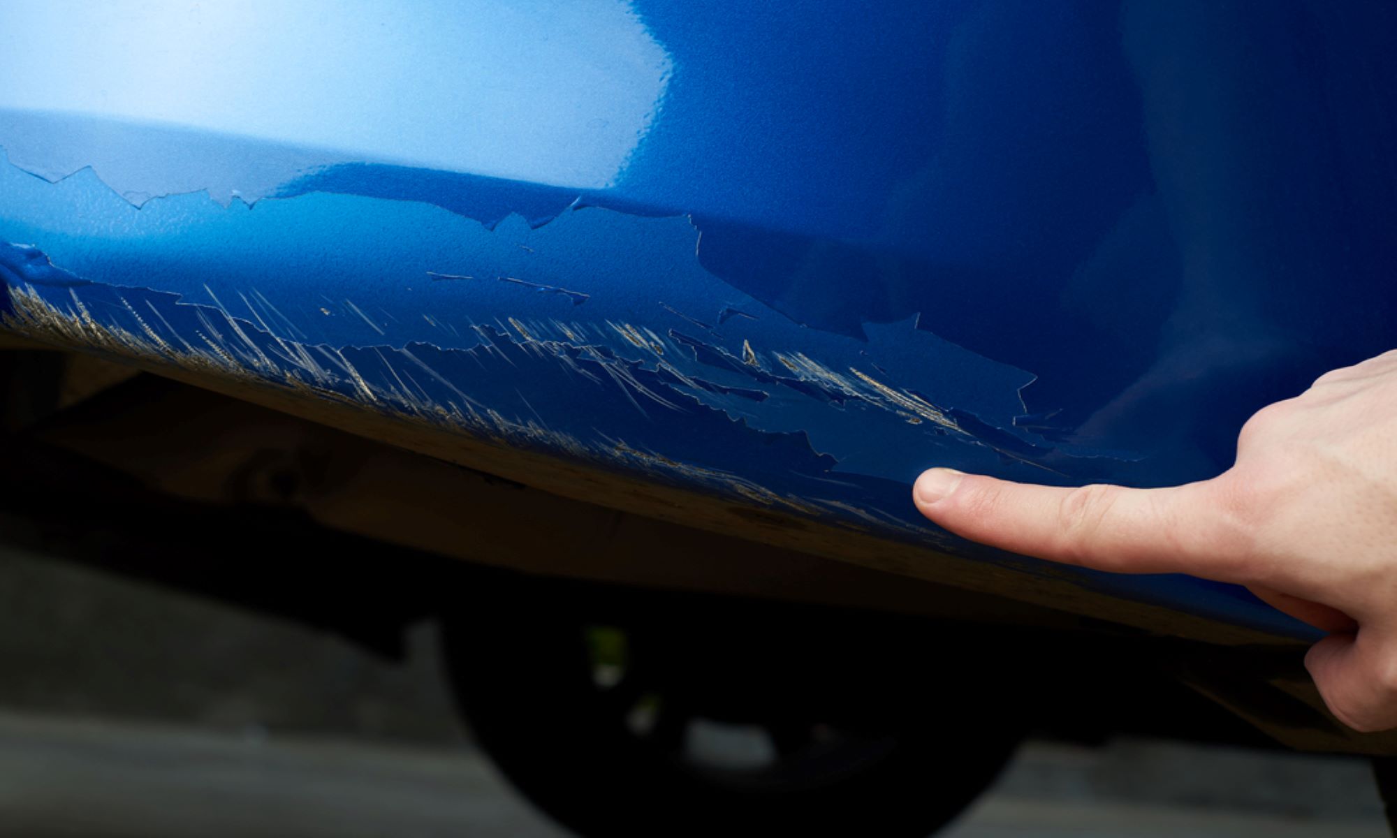 close up view of  chipped blue car paint with owner pointing it out