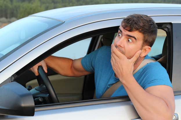 Man with a shocked expression on his face leaning out of his driver's side window with his hand cupped over his mouth.