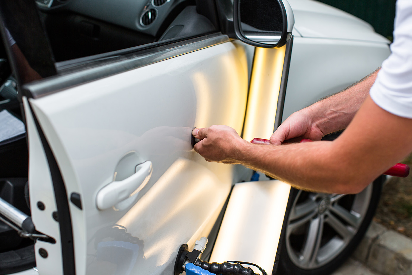 A mechanic shining lights on a white car door to see and repair the dents using PDR.
